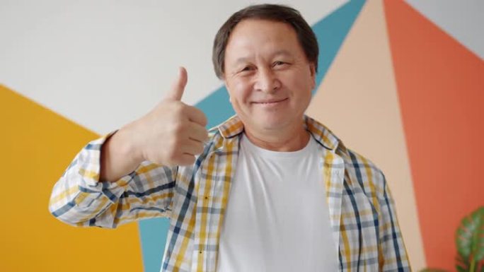 快乐的亚洲成熟男人在彩色背景上用竖起大拇指的手势微笑