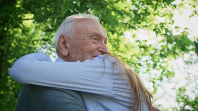 在阳光明媚的日子里，在绿色公园里，快乐孙女的慢动作给了她的祖父一个有效的拥抱，以示爱和尊重