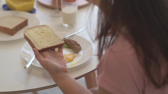 一名亚洲中国女性在餐厅早餐时用黄油刀在面包上涂抹黄油