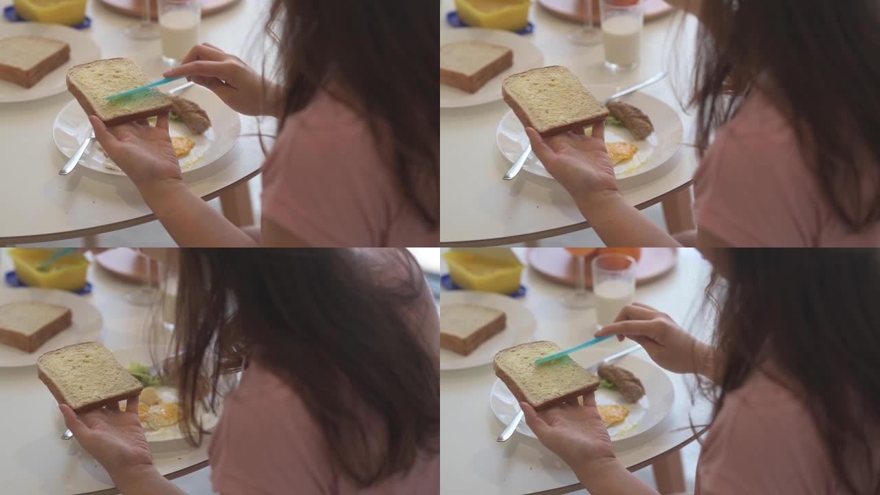 一名亚洲中国女性在餐厅早餐时用黄油刀在面包上涂抹黄油