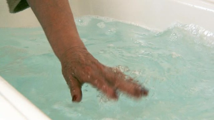 老年妇女触摸热水浴缸的手。