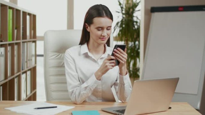 女性在办公室办公桌前使用智能手机的手