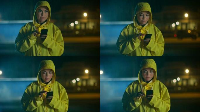 穿着黄色雨衣的美丽年轻女孩正在雨中行走和使用智能手机。她有一个温柔的微笑。天气多雨，现在是晚上。