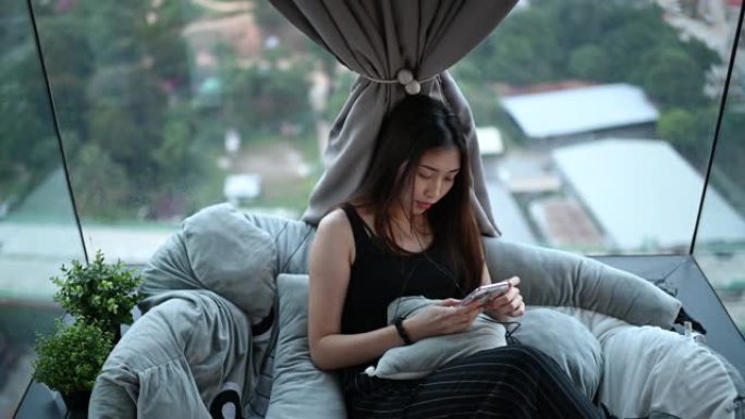 一名亚洲华裔年轻女子在公寓拐角处用手机听音乐