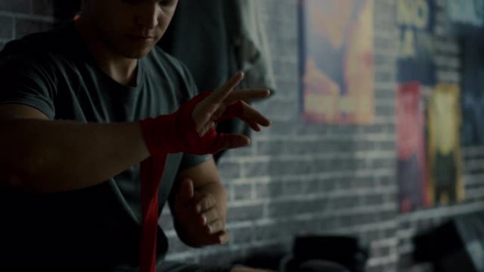 强壮的男性用手包着双手，在健身房里开始跆拳道锻炼，墙上贴有激励人心的海报。他在手腕，拇指和指关节上使