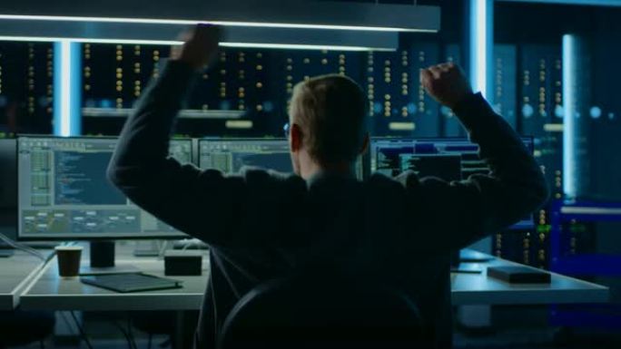 IT专家在带有显示编码语言程序的监视器的个人计算机上工作，他以 “是” 的手势举手来庆祝自己的成功。