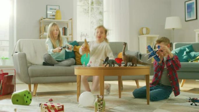 在家: 可爱的女孩在视频游戏机上玩，使用操纵杆控制器，她的年轻兄弟玩玩具飞机，最小的妹妹玩玩具恐龙。