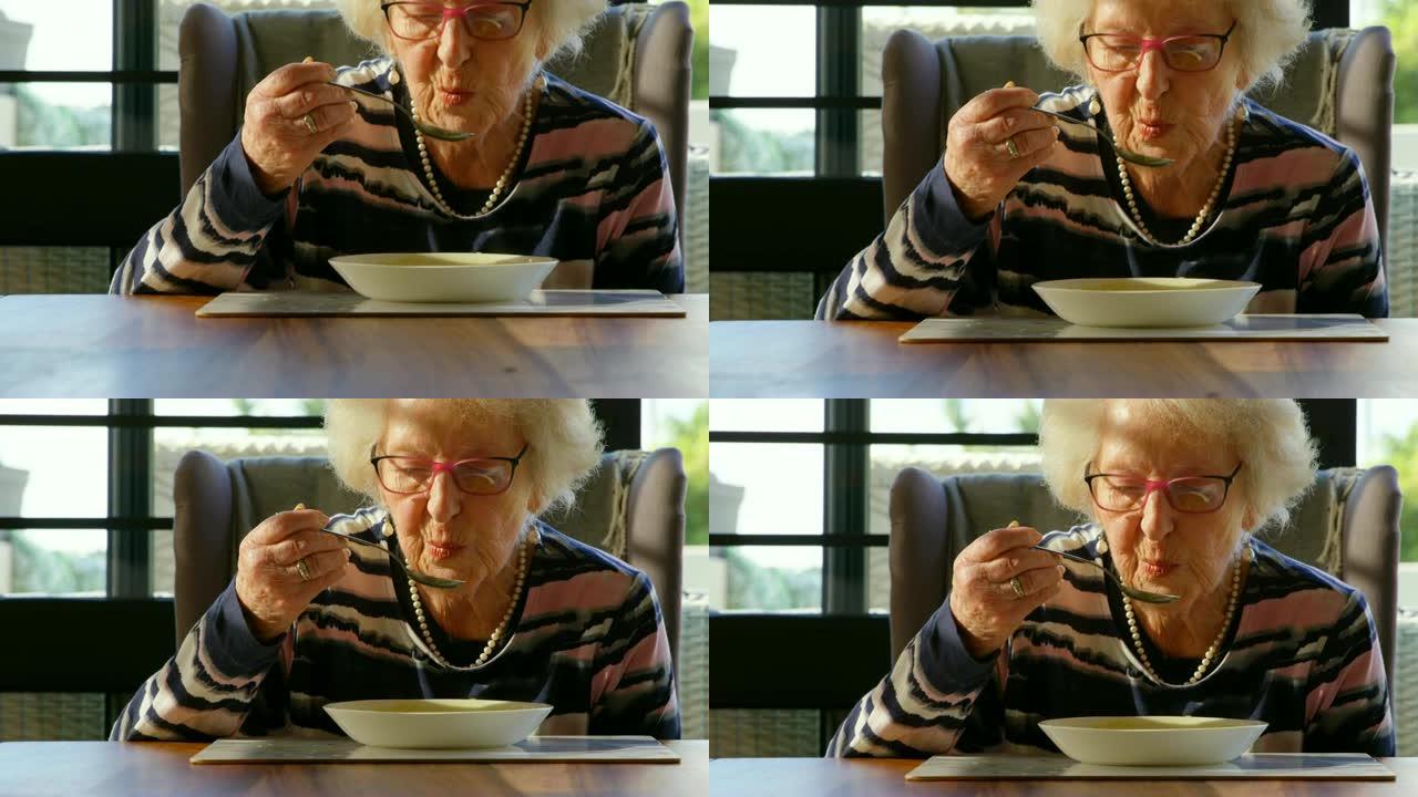 高级妇女在家里的餐桌上喝汤4k