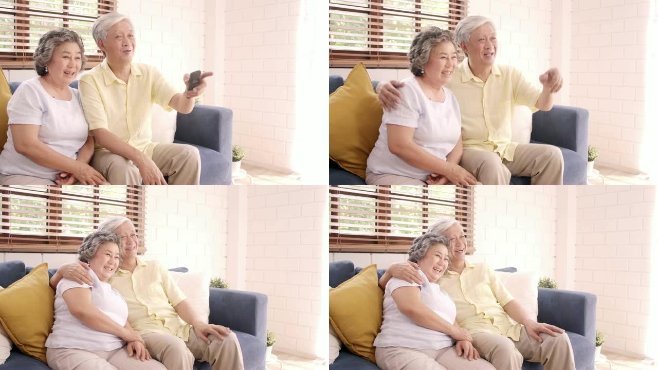 亚洲老年夫妇在家客厅看电视，甜蜜的夫妇在家放松时躺在沙发上享受爱情时刻。享受时间生活方式老年家庭在家
