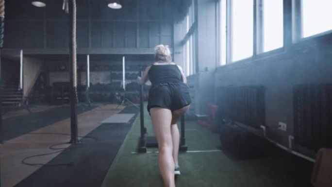 意志力和动力，镜头跟随年轻的运动女子在健身房慢动作中推动重型训练雪橇训练。