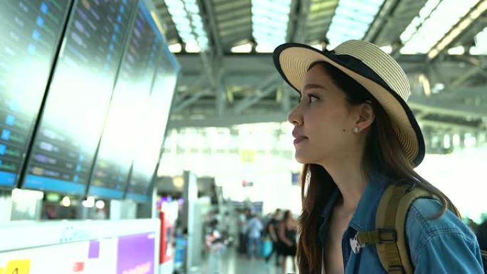 那个年轻的休闲女人在候机楼机场看着航班时刻表。年轻女性独自乘飞机旅行。