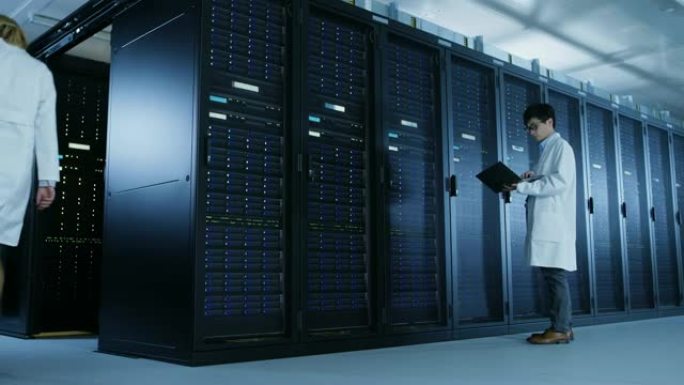 在数据中心: 穿着白大褂的男it技术人员站在开放式服务器机架机柜上，使用笔记本电脑运行维护诊断工具。