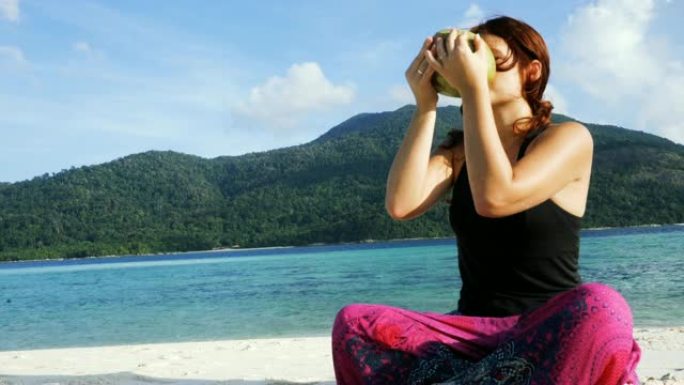 女人喝新鲜的椰子水。瑜伽后在海滩上放松