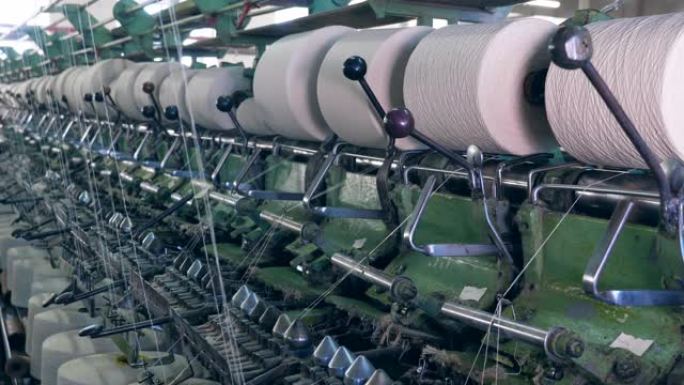 纺织厂的机器与成排的纺纱线轴一起工作。工业纺织厂。