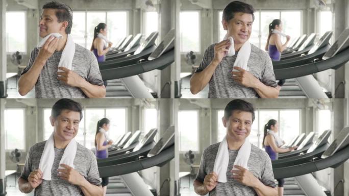 微笑的男人在健身房用餐巾纸擦汗