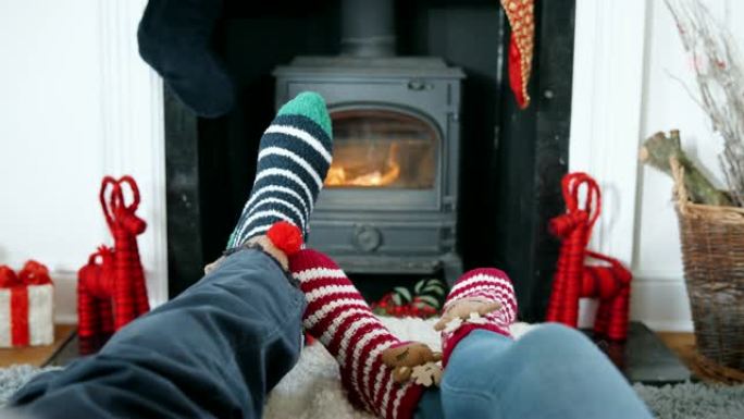 穿着圣诞袜的高级夫妇在燃木炉上暖脚的特写