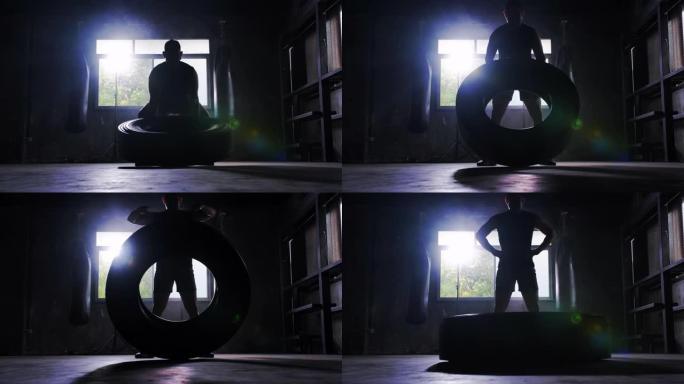 剪影强壮的男人在推轮胎。男人用大轮胎锻炼。在健身房刻苦训练。武术