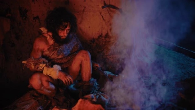 原始穴居人的肖像穿着动物皮坐在他的山洞里，在火附近变暖。原始尼安德特人猎人/智人晚上独自在他的巢穴