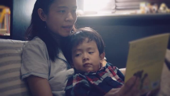 亚洲妈妈和小儿子晚上在床上看书。