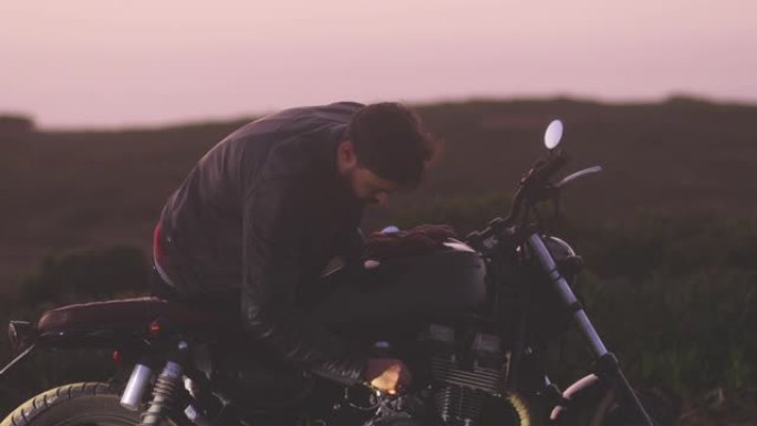 英俊的骑自行车的人在日落时检查经典摩托车