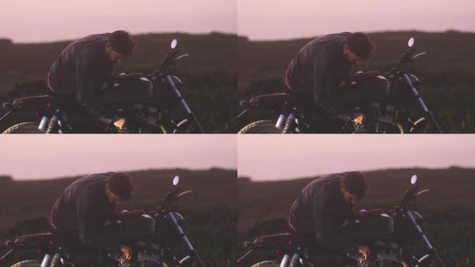 英俊的骑自行车的人在日落时检查经典摩托车