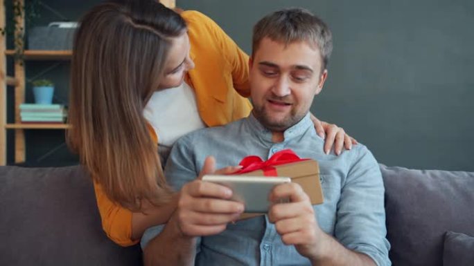 男人在玩智能手机游戏，而妻子给他礼物并在家里接吻