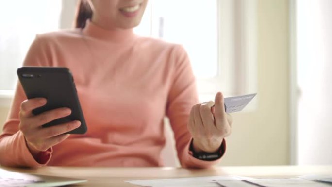 亚洲妇女正在使用带有信用卡的智能手机在线购物