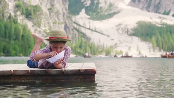 湖边码头上的一个小女孩玩一艘纸船，让她冲浪和吹风，让她旅行。