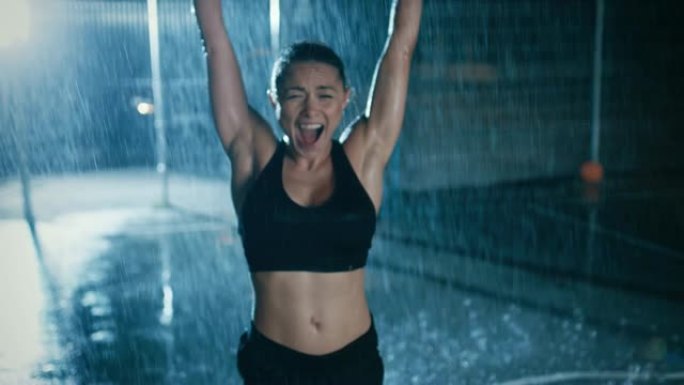 美丽的运动健身女孩正在庆祝她的运动成就。她晚上在大雨中欢呼，身后有一盏灯。