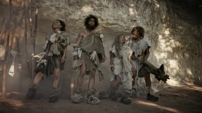由四个狩猎采集者组成的部落，他们戴着动物皮，拿着石尖工具，在他们的洞穴入口处摆姿势。两个成年男性和两