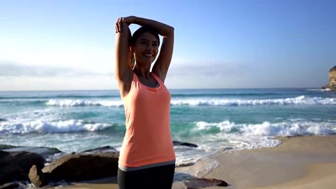站在瑜伽垫上的年轻女子在海滩旁微笑着伸展手臂
