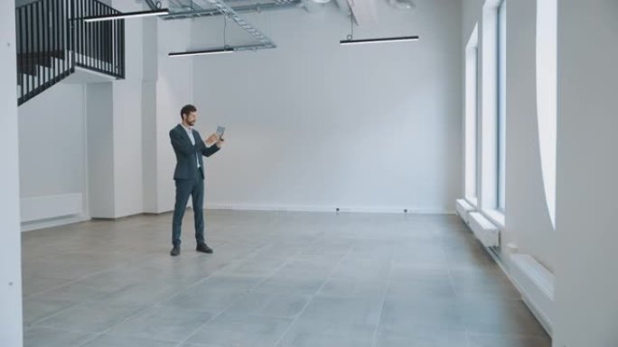 商人站在空荡荡的办公室里，用平板电脑上的增强现实软件来映射它。企业家穿着西装。房间有视频软件的跟踪点