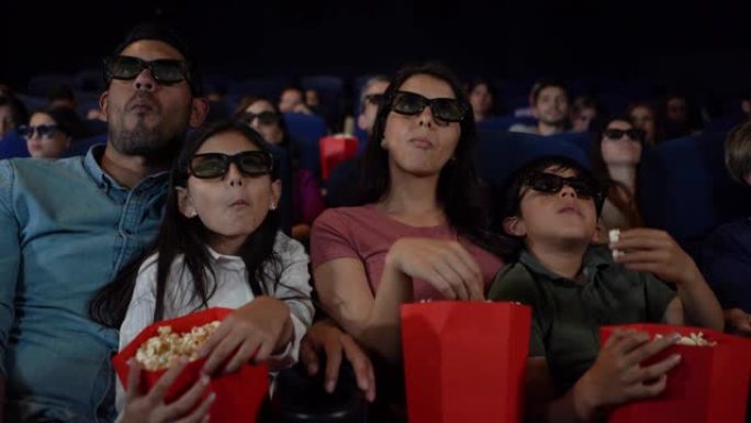 拉丁美洲家庭一边享受3D电影，一边吃零食，看起来很投入
