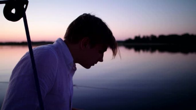 湖上浪漫的日落。年轻人在手机里使用指南针。操纵船