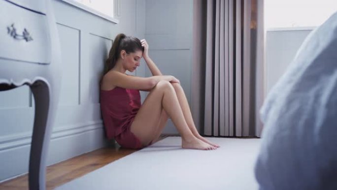 沮丧的女人穿着睡衣坐在卧室的地板上