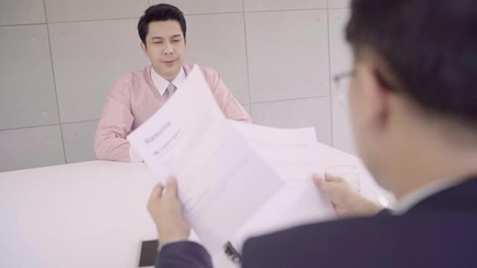 慢动作-有吸引力的年轻亚洲商人在与公司人事经理的工作面试中阅读他的简历。亚洲商人在办公桌前与男性候选