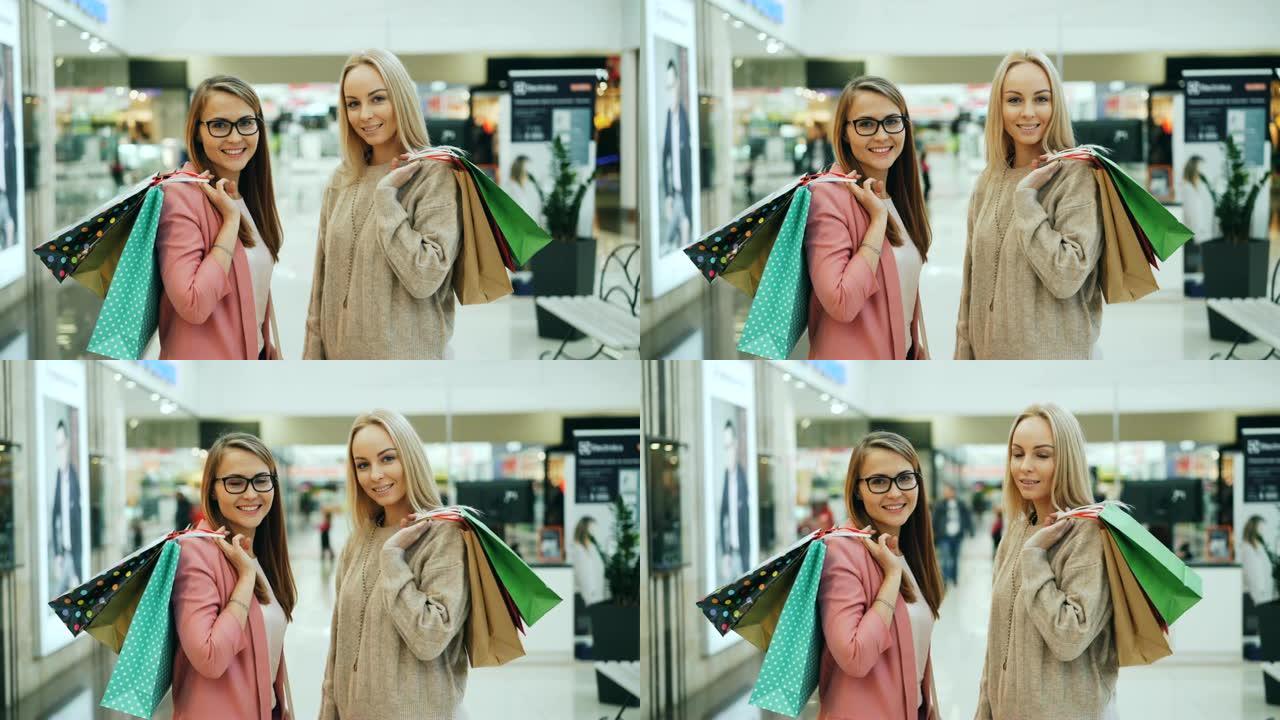大型商店里拿着购物袋的漂亮女孩的肖像看着相机，微笑着。年轻女性穿着时髦的服装和配饰。