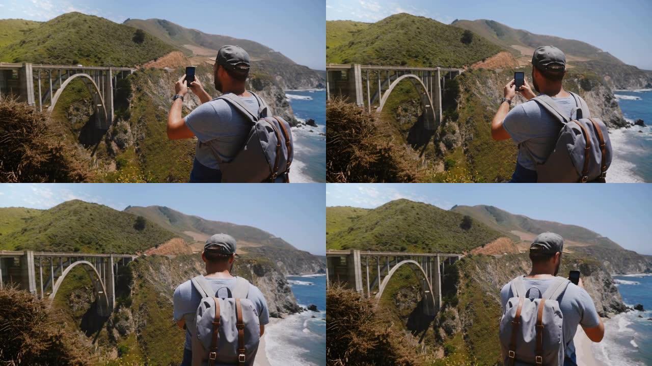 快乐的年轻成人博客作者带背包的游客拍摄美国标志性的比克斯比溪桥全景智能手机视频。