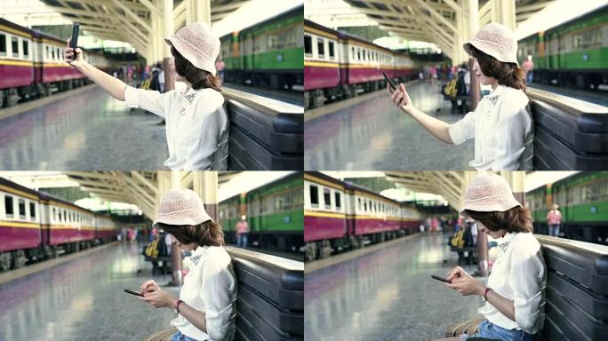 快乐的亚洲女性乘客，在泰国曼谷市的火车站铁轨上，用智能手机随意自拍。生活方式和交通理念。