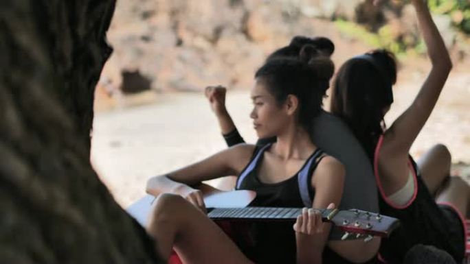 一群享受吉他音乐演奏的女孩。一群朋友在海滩上唱歌。青少年在海边玩得开心。他们在一起聊天和弹吉他。暑假