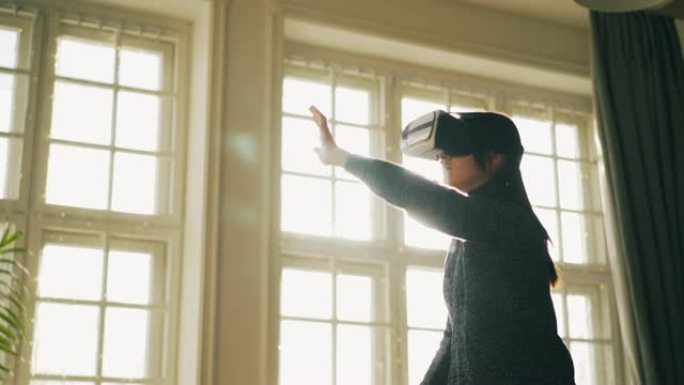 年轻女士正在享受虚拟现实眼镜移动手臂和身体站在房间里戴着ar护目镜的新体验。全景窗口在背景中。