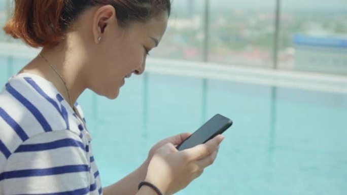 使用智能手机坐在游泳池附近的女性特写镜头，慢动作