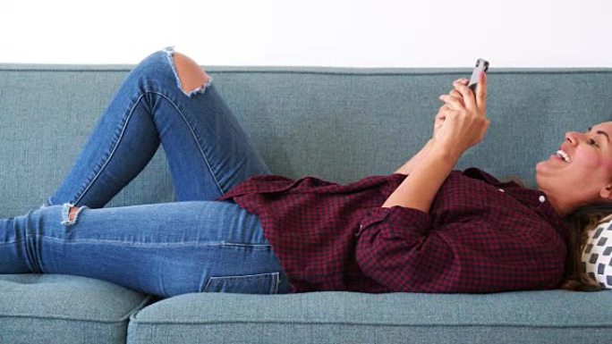 女人在家中躺在沙发上使用手机
