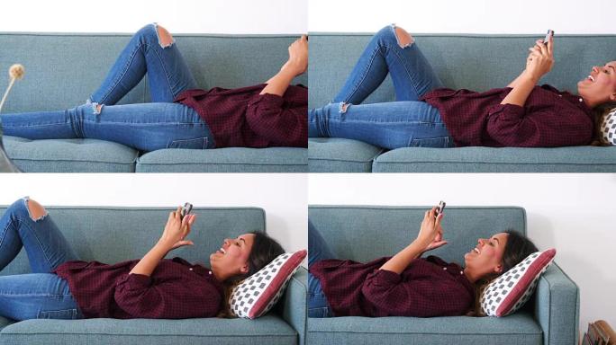 女人在家中躺在沙发上使用手机