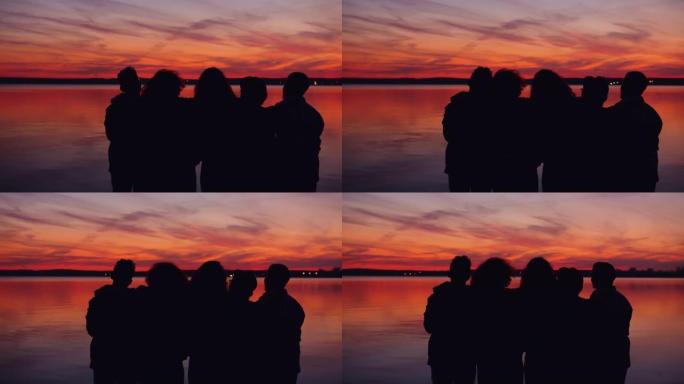 晚上一起站在湖岸看日落的人们的剪影