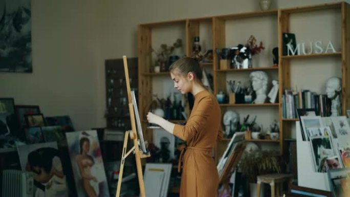 艺术系学生独自在工作室工作，用画笔和调色板站在画架附近的工作室里，用油画绘画。