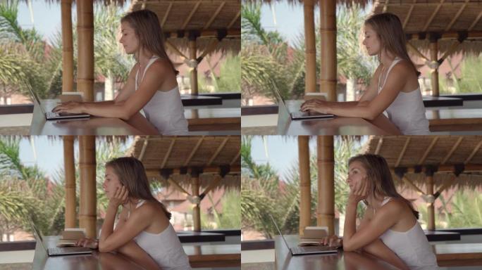 在热带地区的茅草凉亭里在笔记本电脑上工作的女人