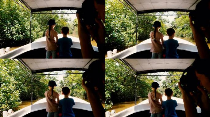 小快乐的女孩和男孩一起在野生动物园游船上沿着异国情调的丛林河航行，年轻的女人给他们拍照。