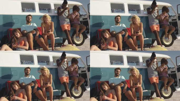 年轻的成年朋友坐在4k海滩上的露营车旁