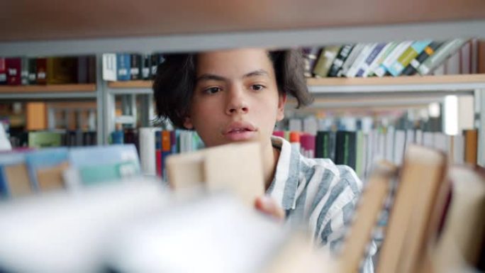 英俊的十几岁男孩学生在大学图书馆选书的特写